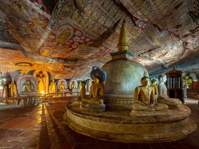 Boeddhabeelden en stupa in de Dambulla-grottempel, Sri Lanka, met kleurrijke plafondschilderingen.