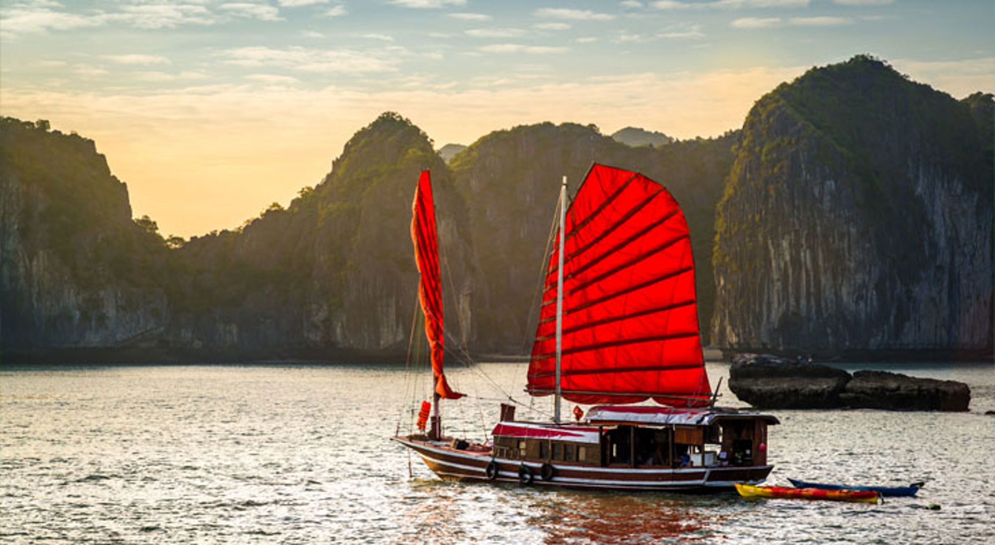 Ha Long Bay Traditionele boot met rode zeilen in Halong Bay, Vietnam, met kalkstenen rotsen op de achtergrond.