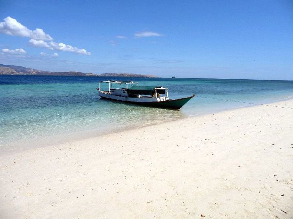 Traditionele boot voor anker bij wit zandstrand en helderblauwe zee op de Kleine Sunda-eilanden, Indonesië.