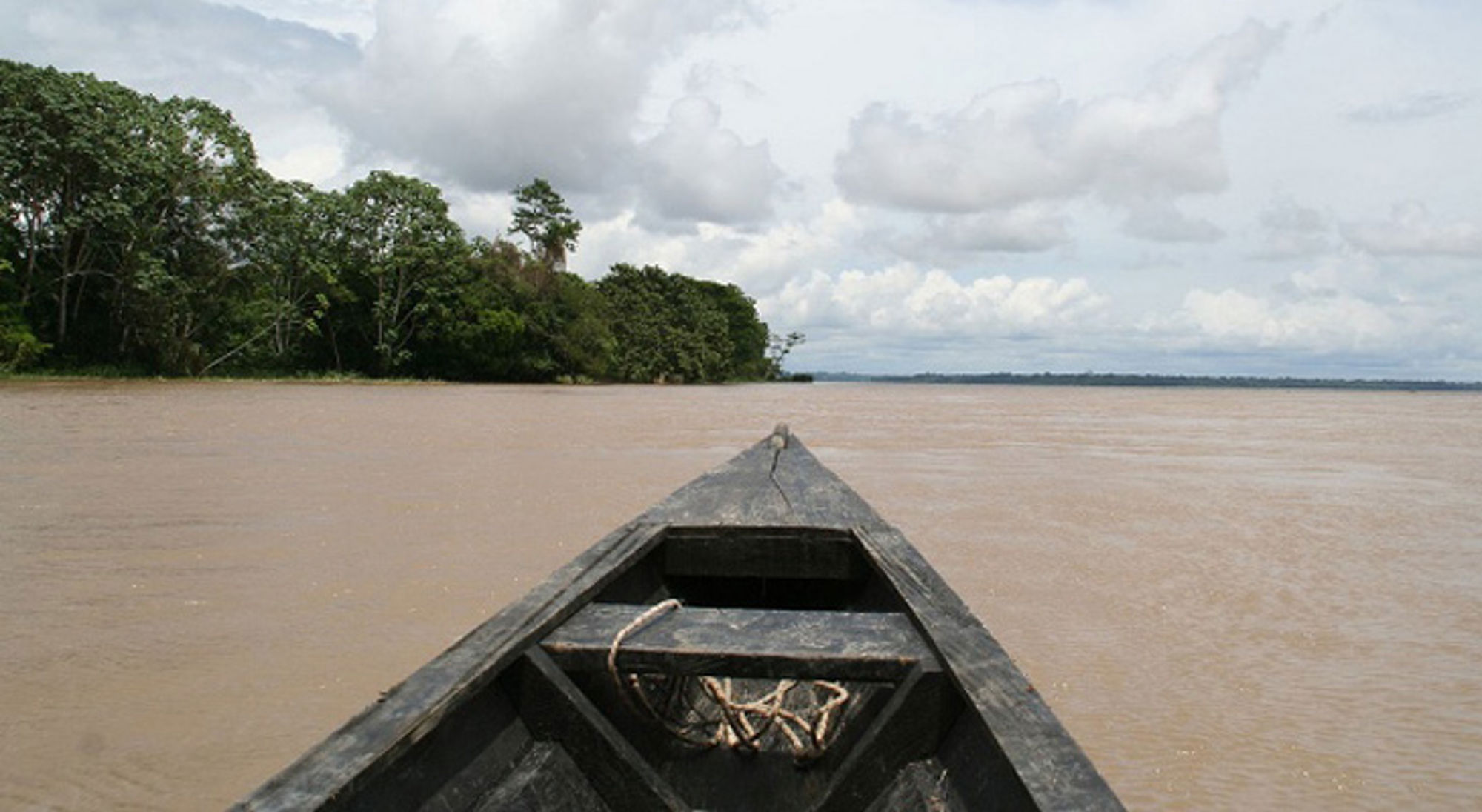 Boottocht Amazone Houten kano op een brede rivier met regenwoud langs de oever in Colombia.