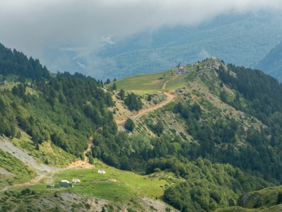 Berglandschap op de Balkan-route met kronkelend pad naar een berghut op een groene bergkam, omringd door bossen.