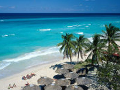 Palmen en parasols op een wit zandstrand aan de turquoise zee in Cuba.