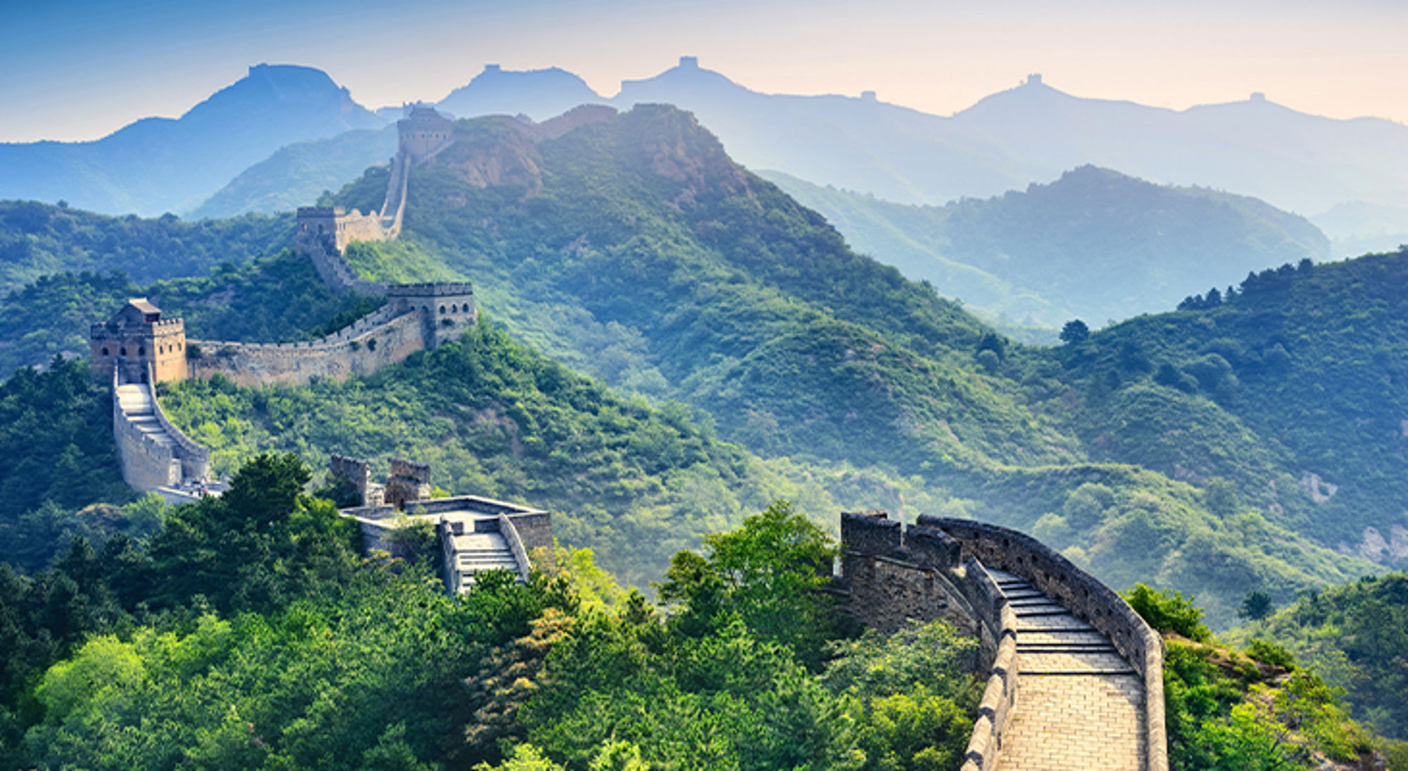 De Chinese Muur slingert over groene bergkammen bij zonsopgang.