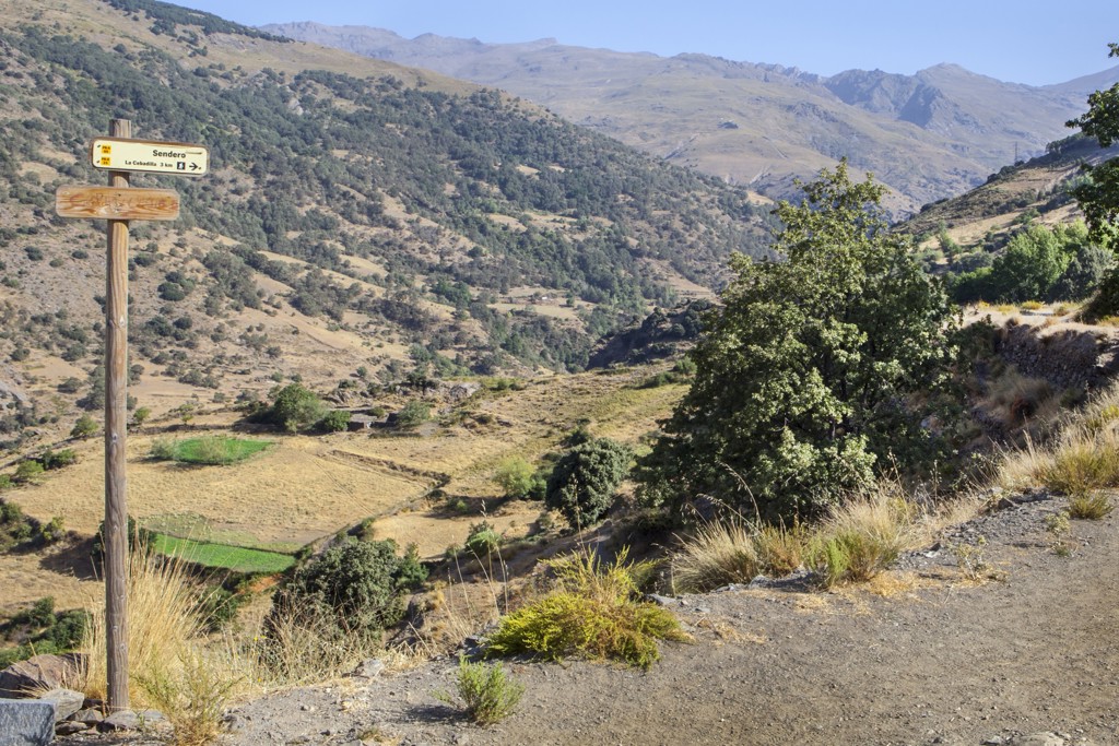 Wandelpad met wegwijzer in de Sierra Nevada bij Granada, met uitzicht op bergvallei en terrassen.