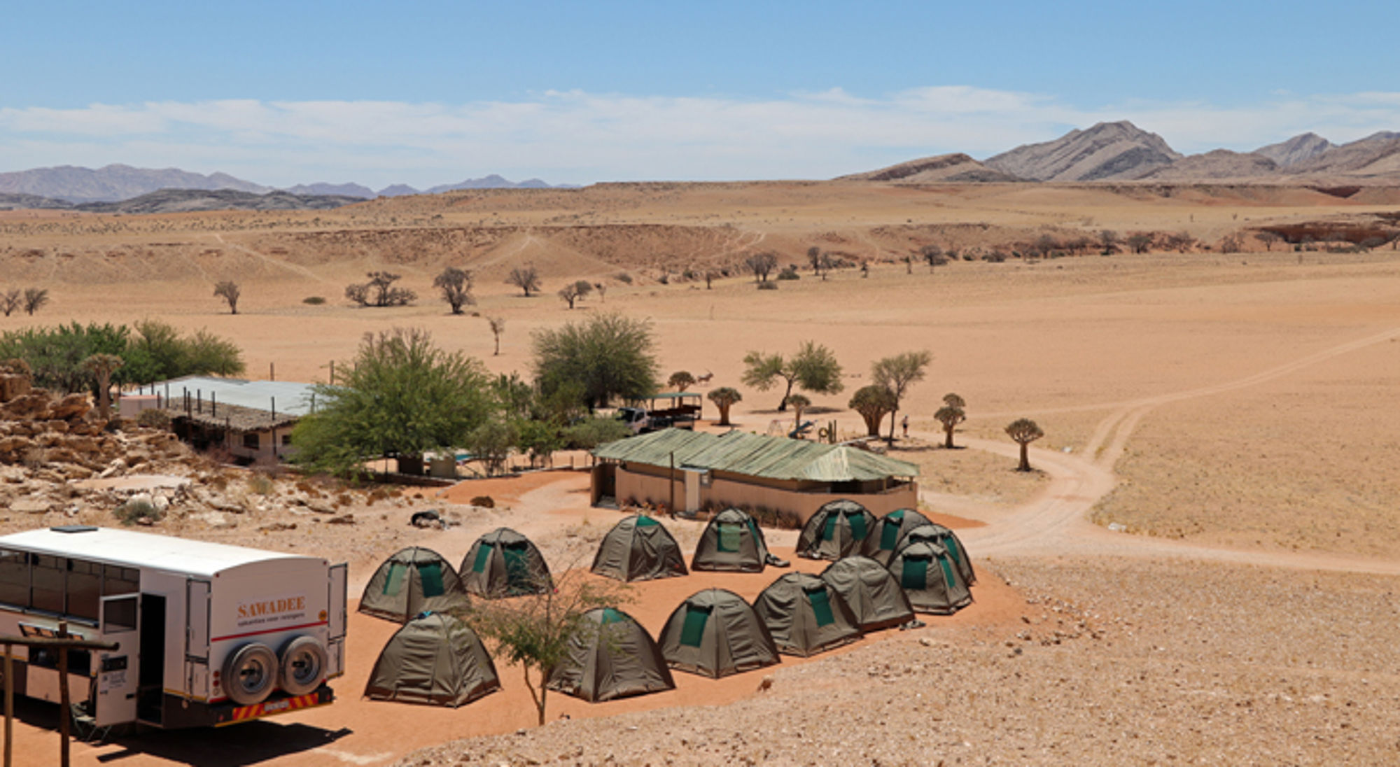 Solitaire kamperen bij Boesman namibie Kampeerterrein met safaritenten in een droog woestijnlandschap, met bergen op de achtergrond.