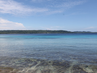 Helderblauwe zee met koraalrif en groene eilandkust op de achtergrond, Molukken.