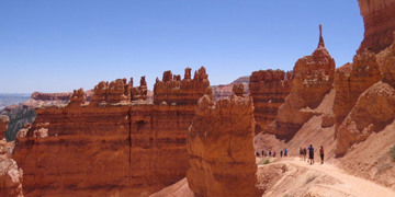 Wandelaars op pad tussen rode rotsformaties in het Wilde Westen, met uitzicht over de canyon.