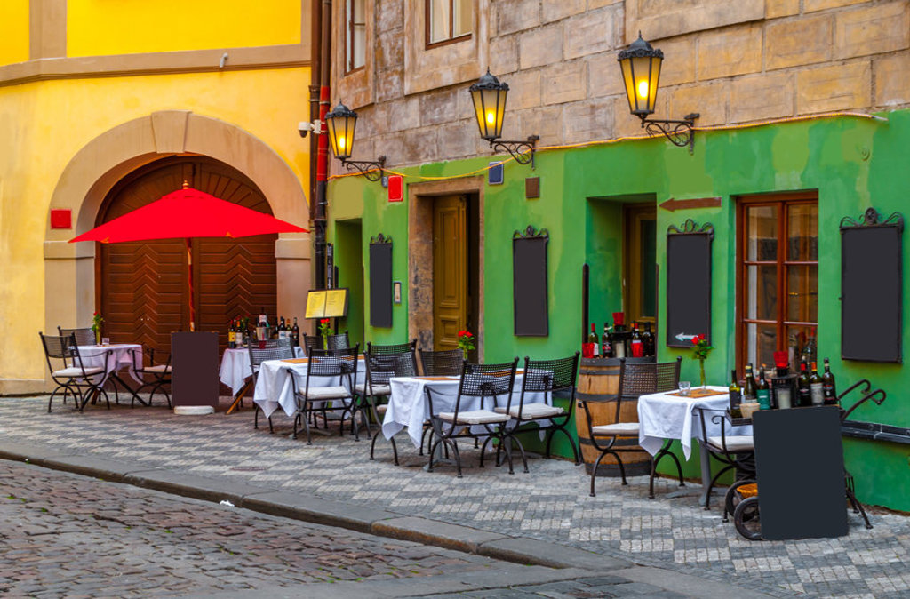 Terras met gedekte tafels en rode parasol in een kleurrijke straat in Praag tijdens fietsvakantie van Praag naar Wenen.