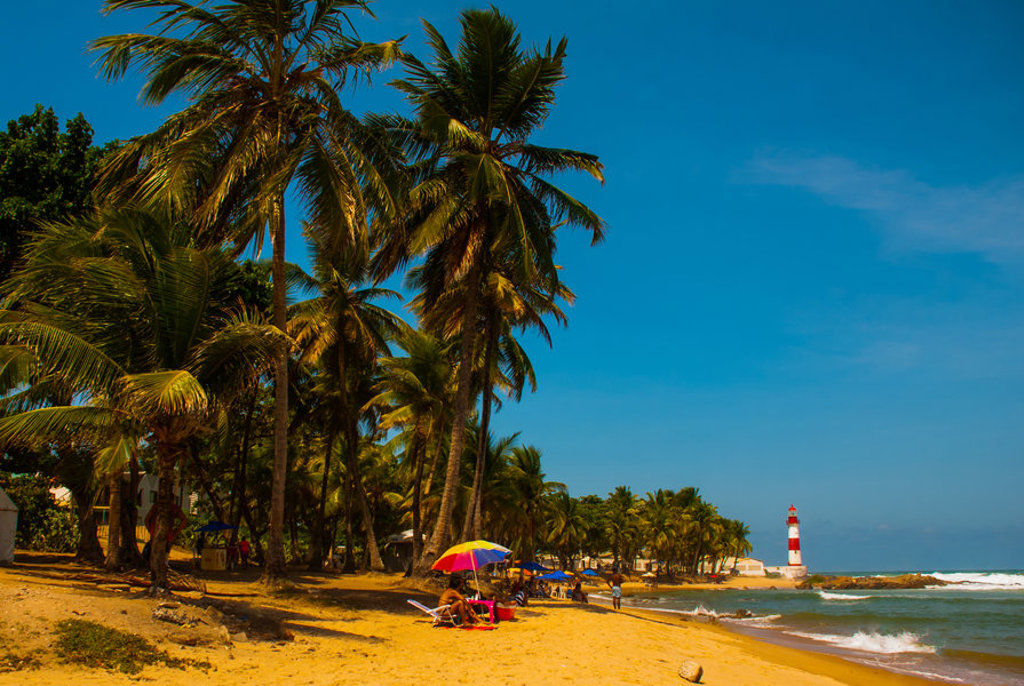 Palmenstrand in Brazilië met kleurrijke parasols en een vuurtoren aan de kust.