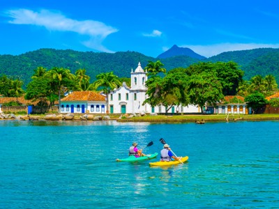 Kajakkers op zee bij Paraty met de witte Igreja de Santa Rita en groene bergen op de achtergrond.