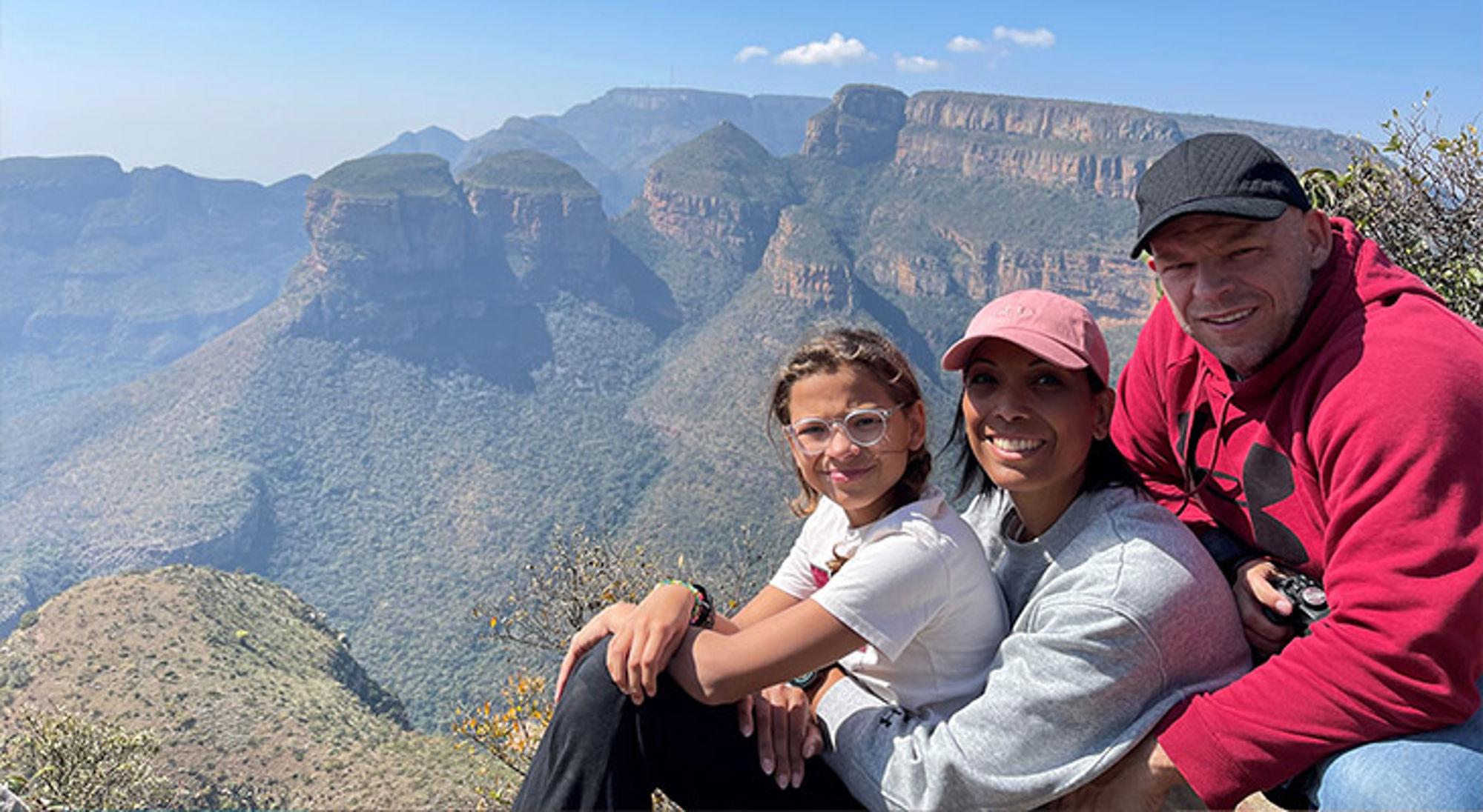 Familiereis Zuid-Afrika Gezin poseert bij uitzichtpunt met berglandschap en diepe kloof op de achtergrond.