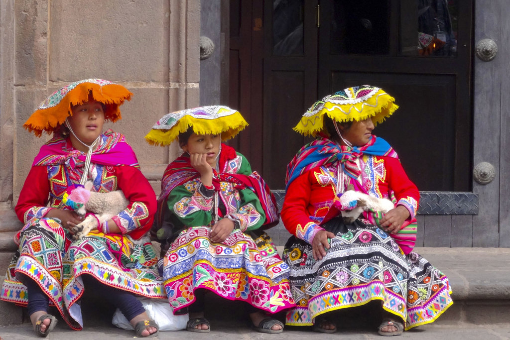 Drie vrouwen in kleurrijke traditionele kleding zitten voor een gebouw in Peru tijdens een rondreis.