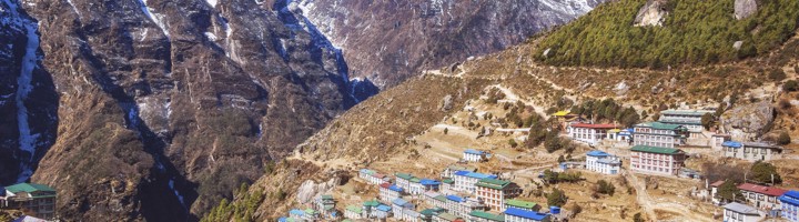 Uitzicht op Namche Bazaar met kleurrijke daken en besneeuwde Himalaya-bergen op de achtergrond.