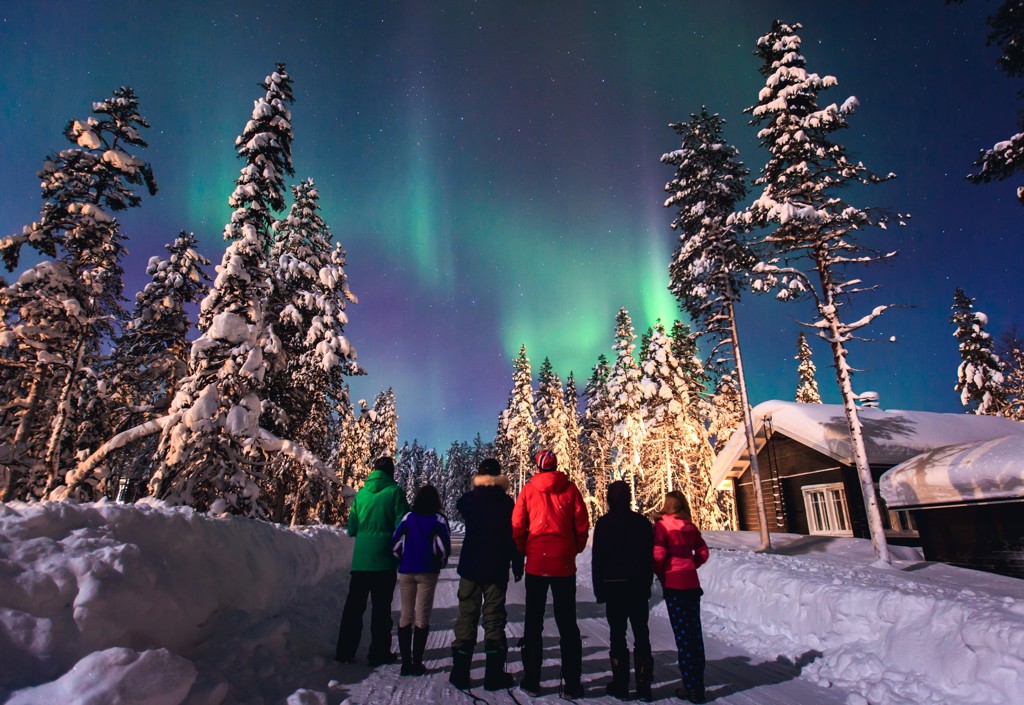 Noorderlicht boven besneeuwd bos en lodge tijdens groepsrondreis Zweeds en Noors Lapland.