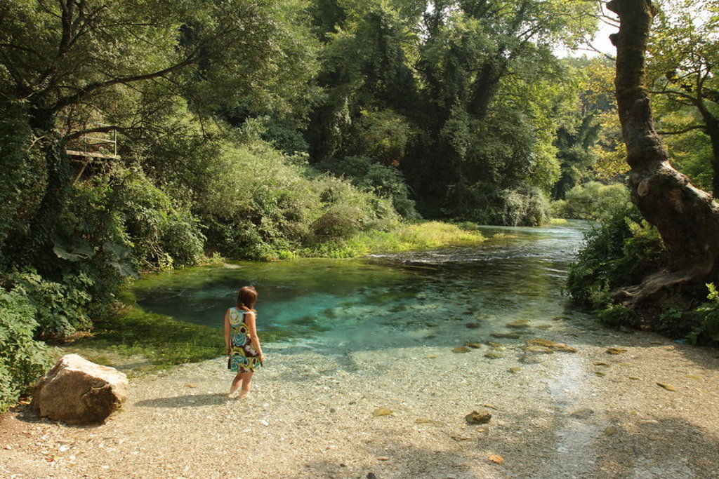 Vrouw bij helderblauwe rivier in groen boslandschap in Albanië.