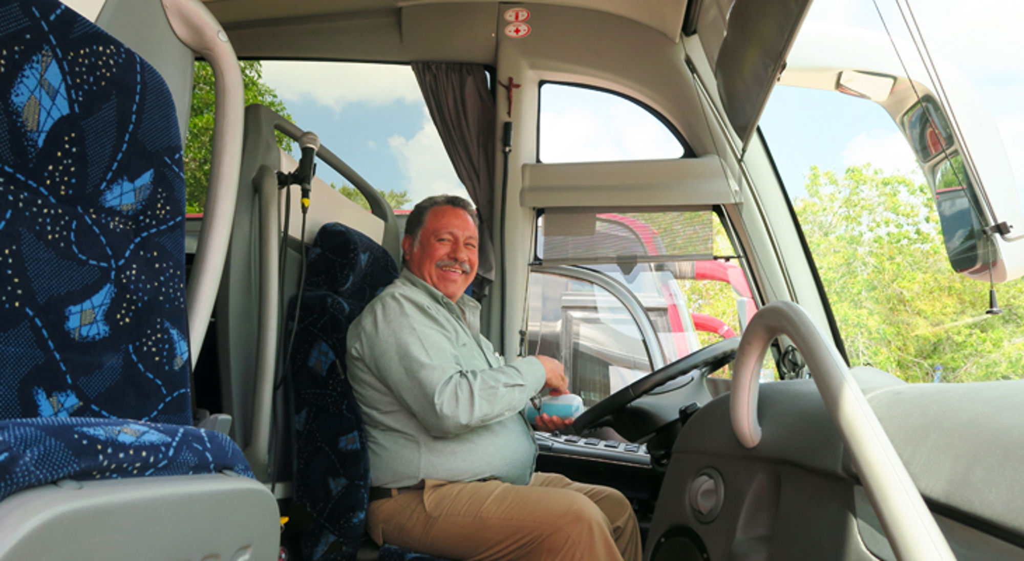 Buschauffeur glimlacht achter het stuur in een touringcar.