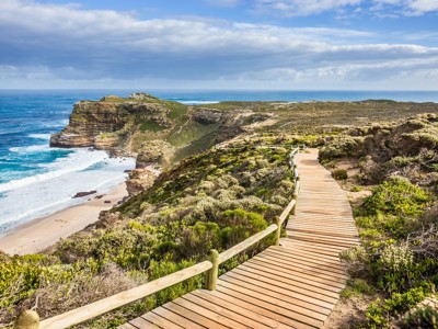 Houten wandelpad langs de ruige kust en kliffen van Zuid-Afrika, met uitzicht op zee en strand.