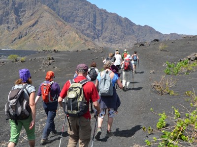 Wandelaars op een zwarte vulkanische route op Kaapverdië, met ruige bergen op de achtergrond.