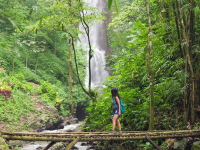 Wandelen door tropisch regenwoud op Bali met bamboebrug en waterval op de achtergrond.
