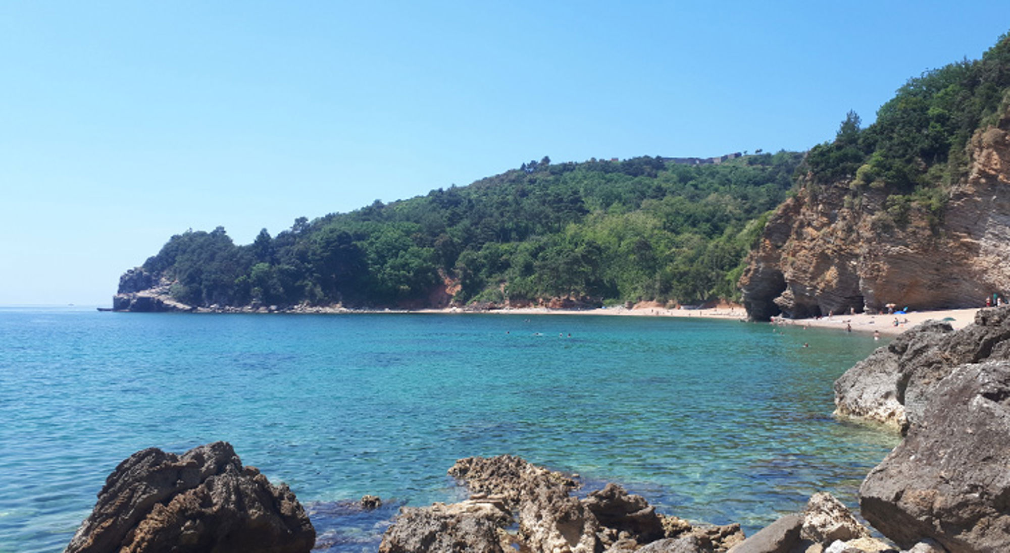 Balkan Rotsachtige baai met helderblauw zeewater, groen beboste heuvels en zandstrand.