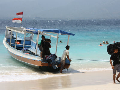 Boot op het strand van de Kleine Sunda-eilanden met Indonesische vlag en reizigers die zwemmen in zee.