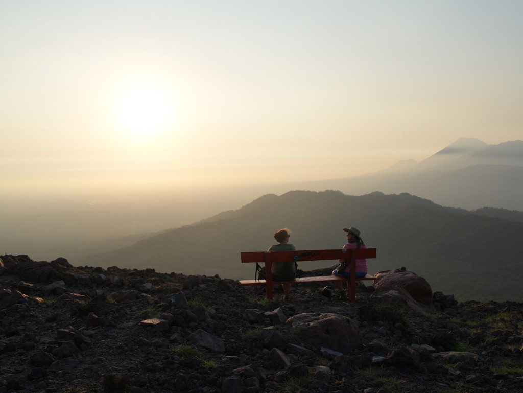 Reizigers op een bankje met uitzicht op vulkanisch berglandschap bij zonsondergang in Nicaragua.