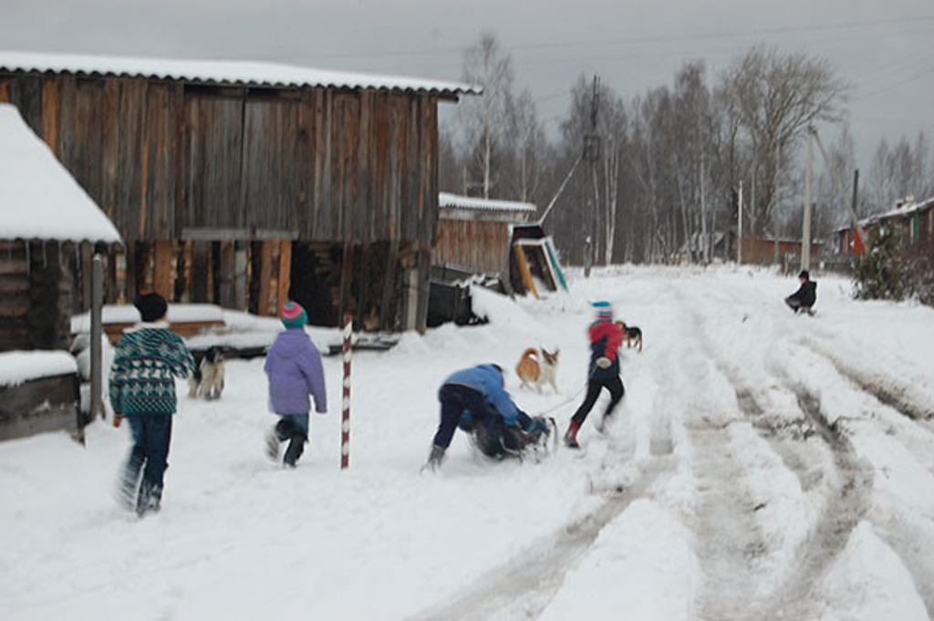 Kinderen spelen in de sneeuw bij houten huizen in een Russisch dorp tijdens de winterrondreis.