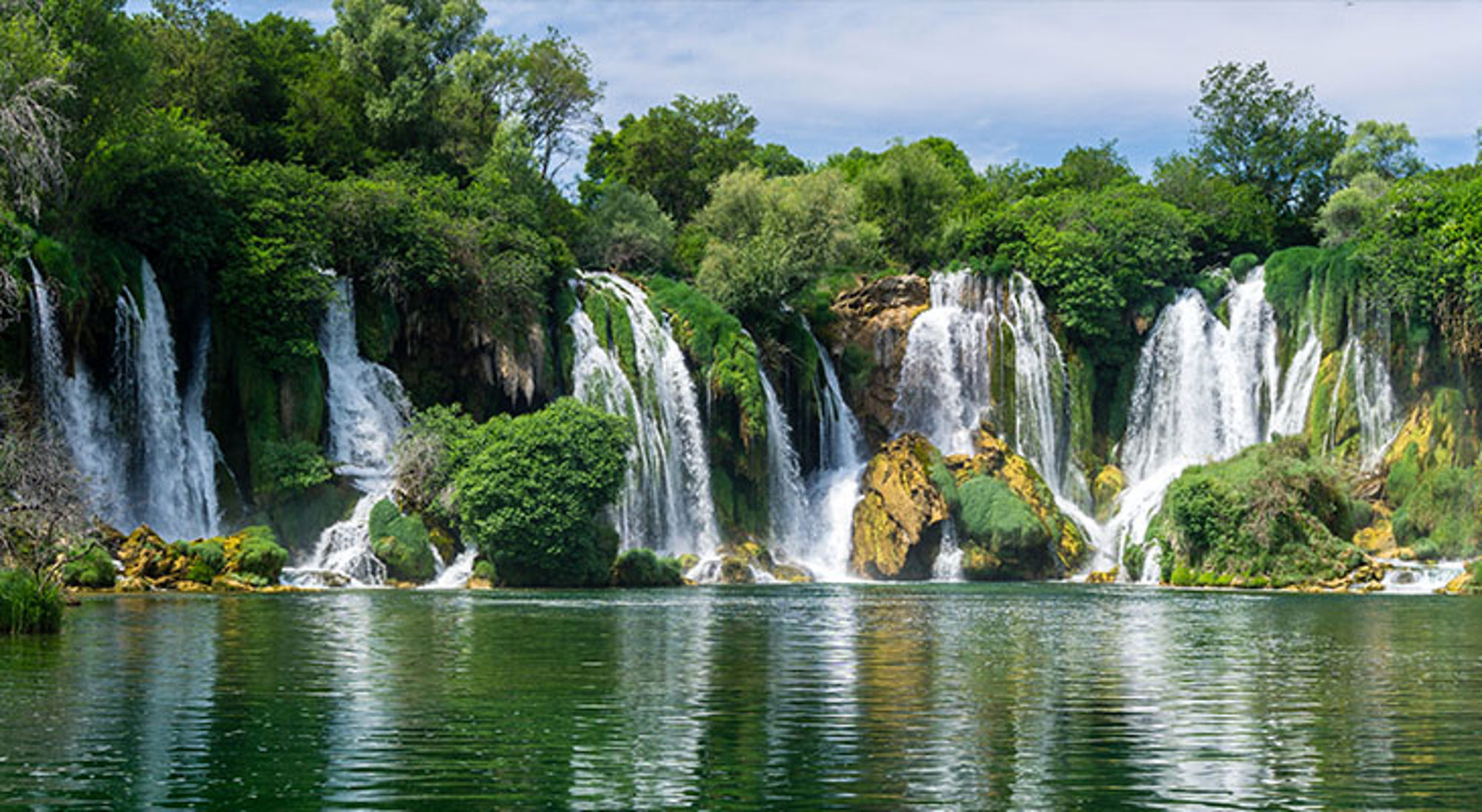 Kravica waterfalls Watervallen stromen door groen begroeide rotsen in een brede rivier.