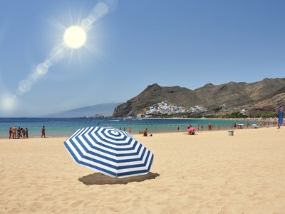 Zandstrand op de Canarische Eilanden met parasol, zwemmers en bergen met kustdorp op de achtergrond.