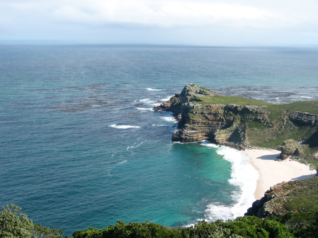 Uitzicht op rotsachtige kustlijn met turquoise zee en zandstrand tijdens groepsrondreis Zuid-Afrika, eSwatini en Lesotho.