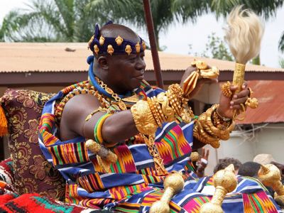 Traditionele ceremonie in Ghana met man in kleurrijke kente en gouden sieraden tijdens groepsrondreis Ghana, Togo en Benin.