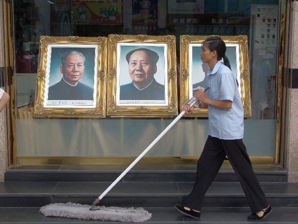 Schoonmaakster dweilt voor etalage met portretten in een Chinese stad tijdens een familiereis China.