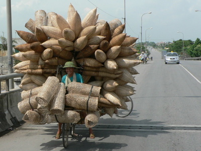 Fietser in Vietnam met enorme lading rieten manden op een brug tijdens de Route Vietnam.