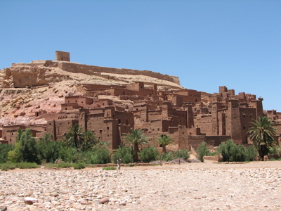 Kasbah Aït Ben Haddou langs de route Marokko familiereis, met lemen gebouwen en palmbomen onder blauwe lucht.