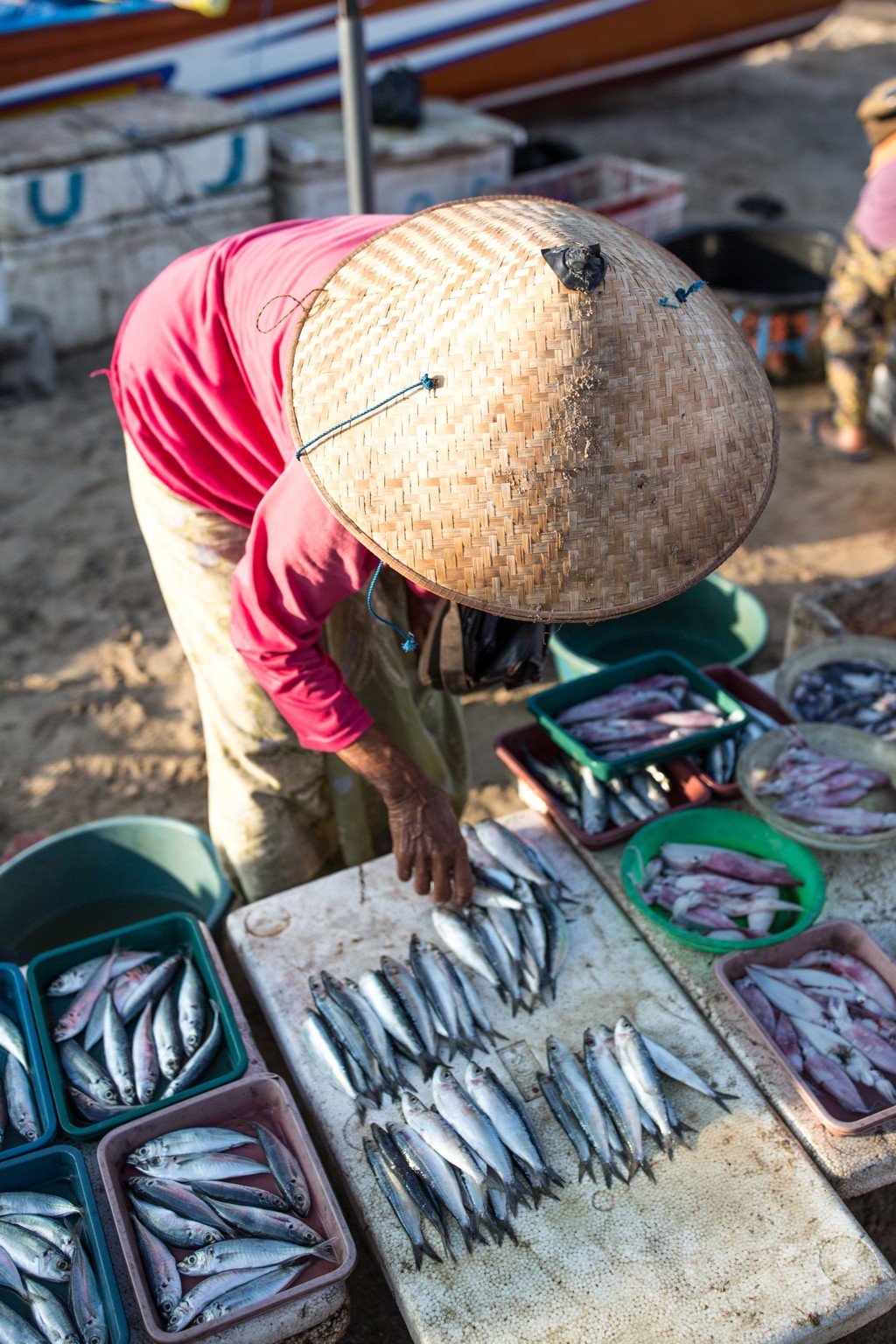 Visverkoper met rieten hoed sorteert verse vis op een markt tijdens de rondreis Timor, Sumba & Bali.