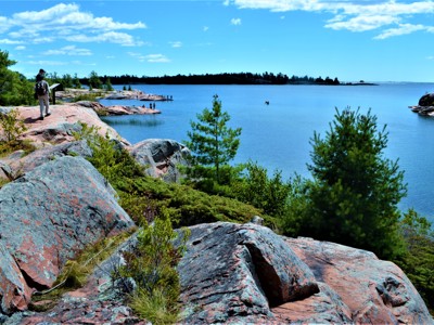Wandelaars op rotsachtige kust bij Georgian Bay in Oost-Canada, met dennenbomen en helderblauw water.