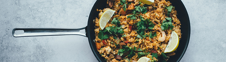 Paella met garnalen, citroenpartjes en verse kruiden in een pan.