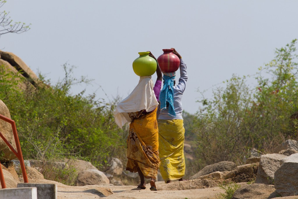 Twee vrouwen lopen over een pad in Gujarat, India, met waterpotten op hun hoofd.