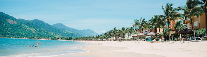 Tropisch strand in Brazilië met palmbomen, zee en bergen op de achtergrond.