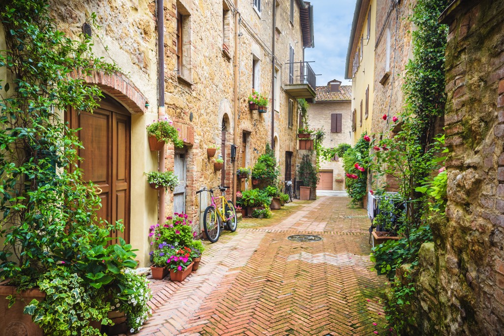 Sfeervol steegje in Toscane met stenen huizen, bloemen en een fiets langs de muur.