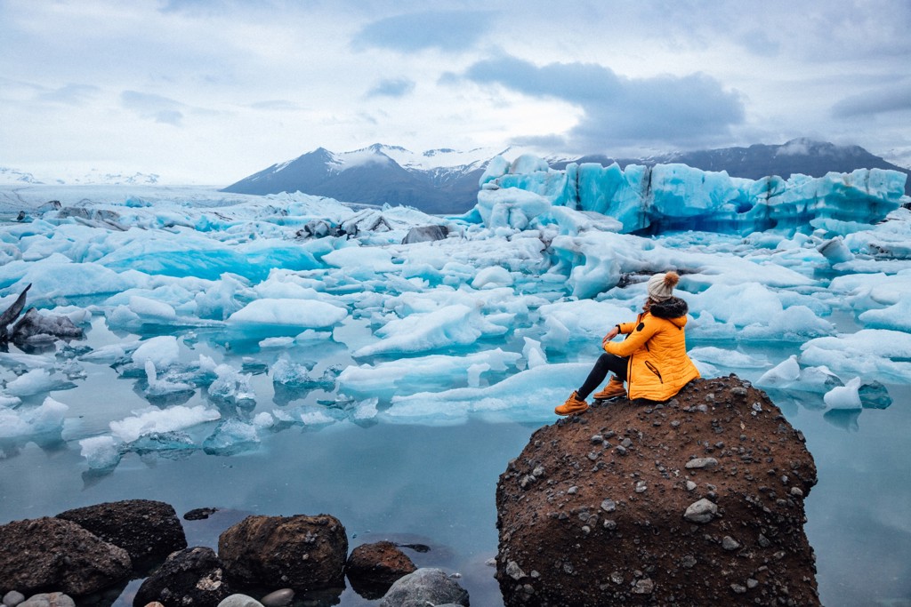 Reiziger kijkt uit over drijvende ijsbergen in de gletsjerlagune Jökulsárlón in IJsland.