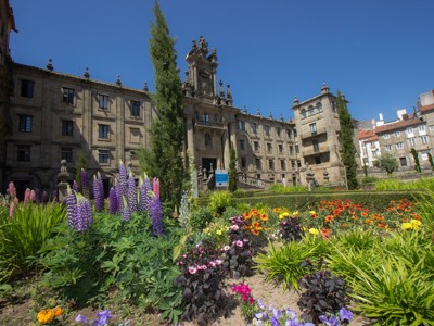 Historisch kloostergebouw in Santiago de Compostela met kleurrijke bloementuin op de voorgrond.