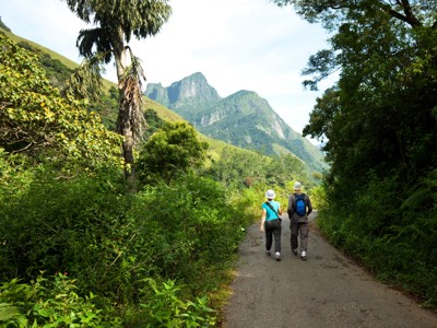Wandelaars op een pad door groen berglandschap in Sri Lanka, met hoge pieken op de achtergrond.