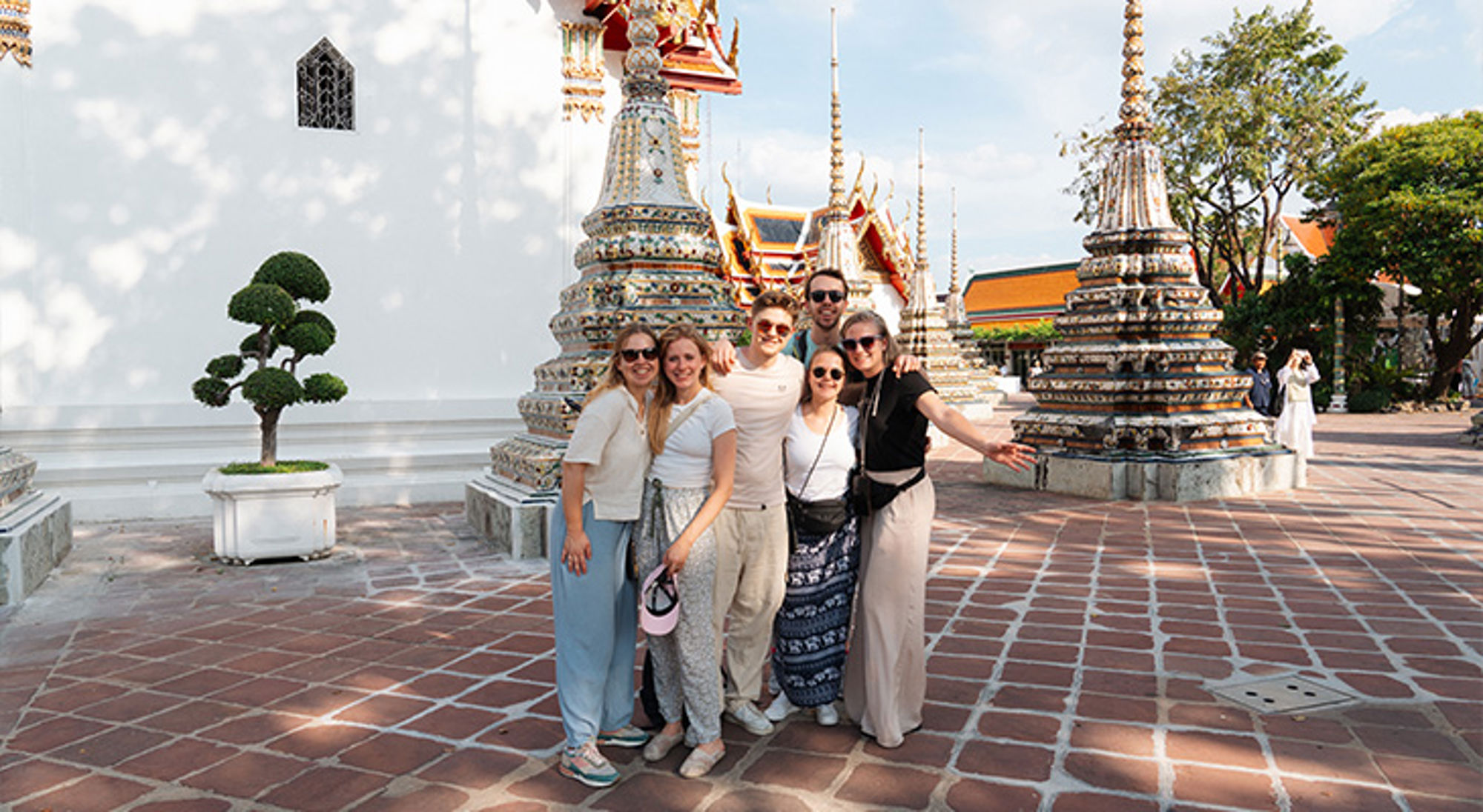 Groep reizigers poseert bij kleurrijke tempelstupa’s in Bangkok, Thailand.
