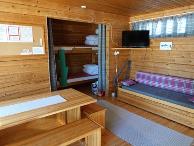 Interieur van een houten hut met stapelbed, eettafel en bank, overnachtingsplek tijdens Route Thailand.