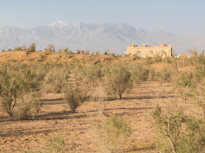 Woestijnlandschap in Iran met struiken, een lemen gebouw en besneeuwde bergen op de achtergrond.