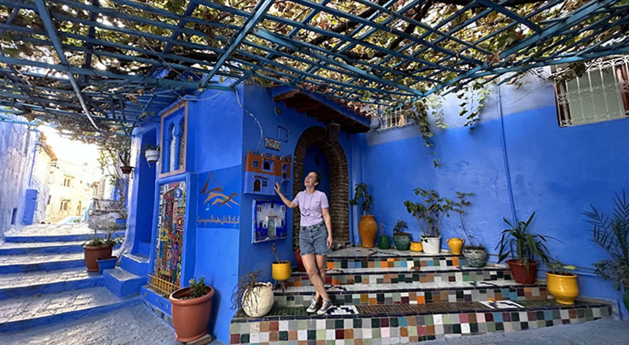 Sara in Marokko Reiziger bij blauw geschilderde straat met mozaïektrap en plantenpotten in Chefchaouen, Marokko.