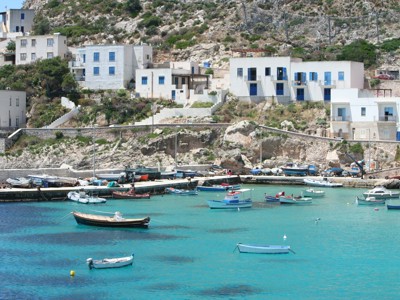 Kleine haven met vissersbootjes en wit-blauwe huizen aan de rotskust van West-Sicilië.