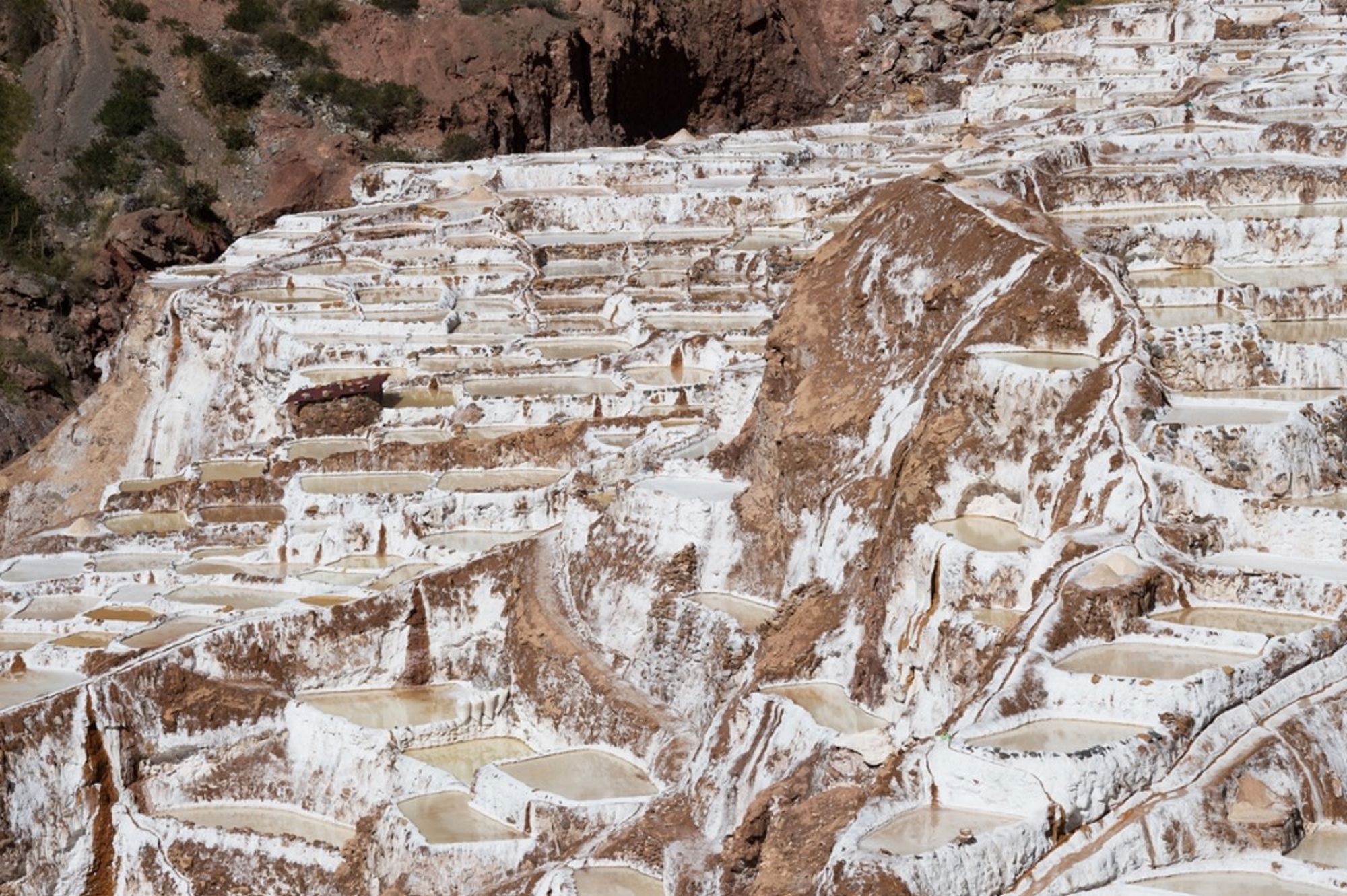 Zoutterrassen van Maras bij Cusco, Peru, met witte terrassen en waterbassins op een berghelling.