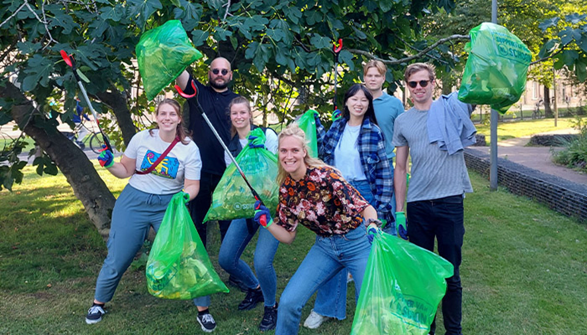 Carolien en collega's tijdens World Cleanup Day Vrijwilligers ruimen zwerfafval op in het park met grijpers en groene afvalzakken.